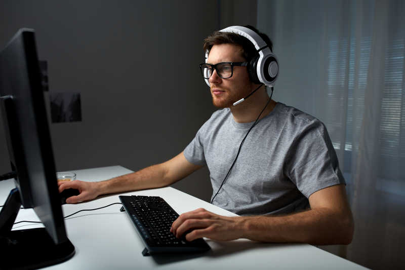 戴着耳机和眼镜在家玩电脑的男人