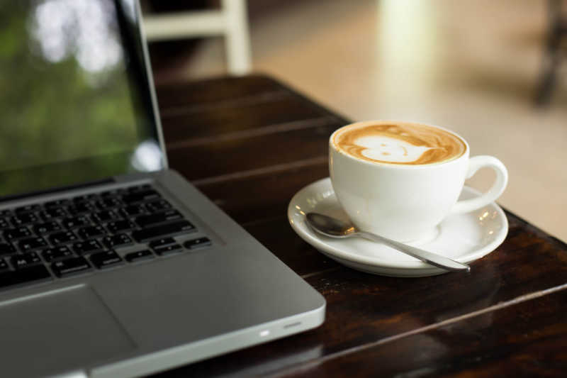 木制桌子的笔记本电脑和热拿铁咖啡