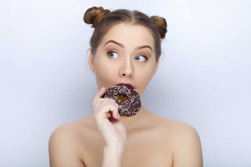 白色背景下用甜甜圈搞怪的可爱女孩