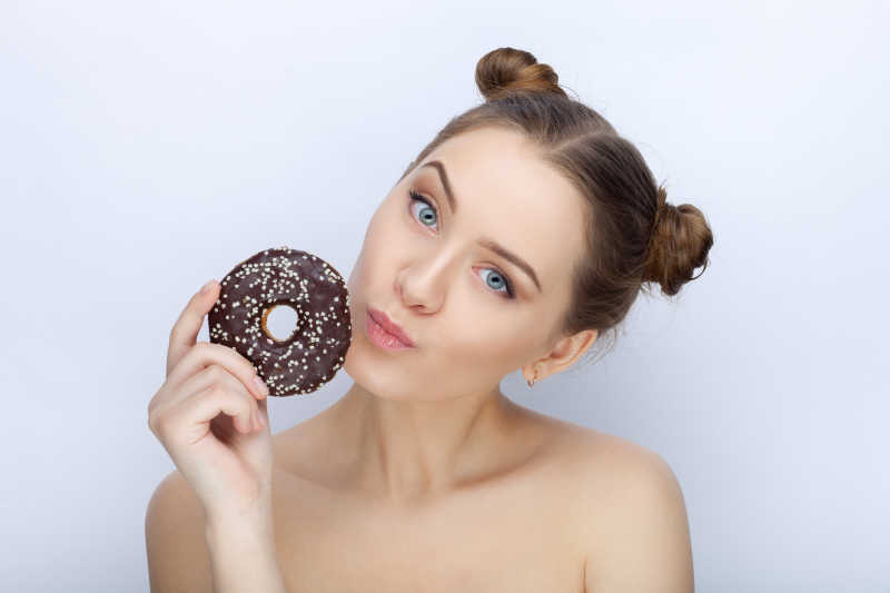 白色背景下拿着黑色甜甜圈的可爱女孩