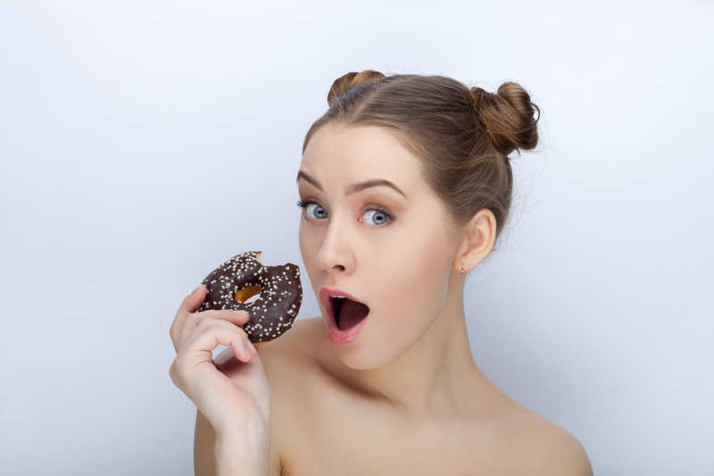 白色背景下拿着甜甜圈的美丽女孩