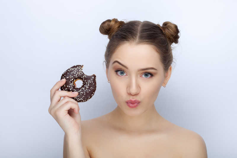 白色背景下举着甜甜圈搞怪的女孩
