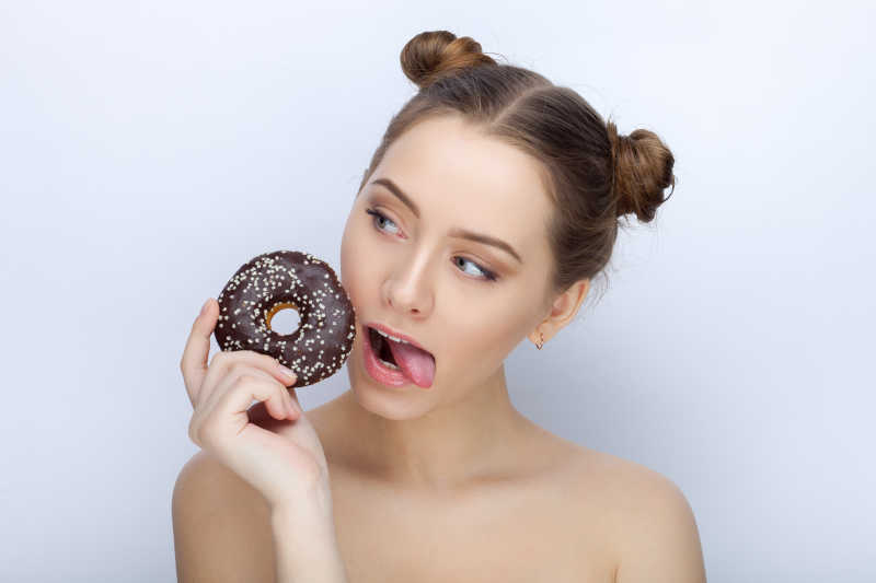 白色背景下对着甜甜圈搞怪的女孩