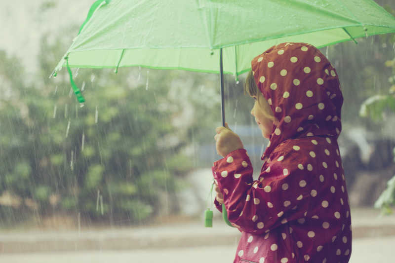 大雨中一个孩子打着绿色的雨水