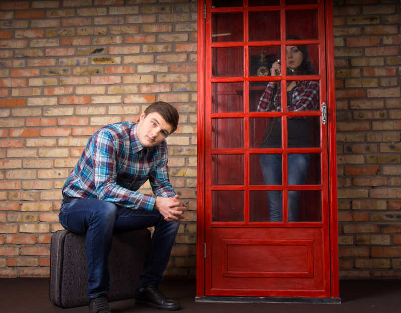 砖墙背景下等待女友打电话的坐在行李箱上的男人