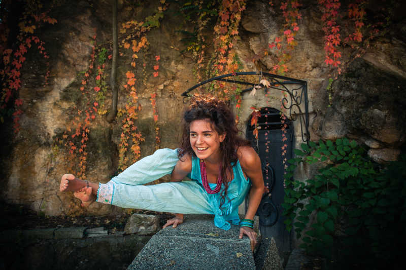微笑的年轻女子在旧墙和悬崖秋日前练习平衡