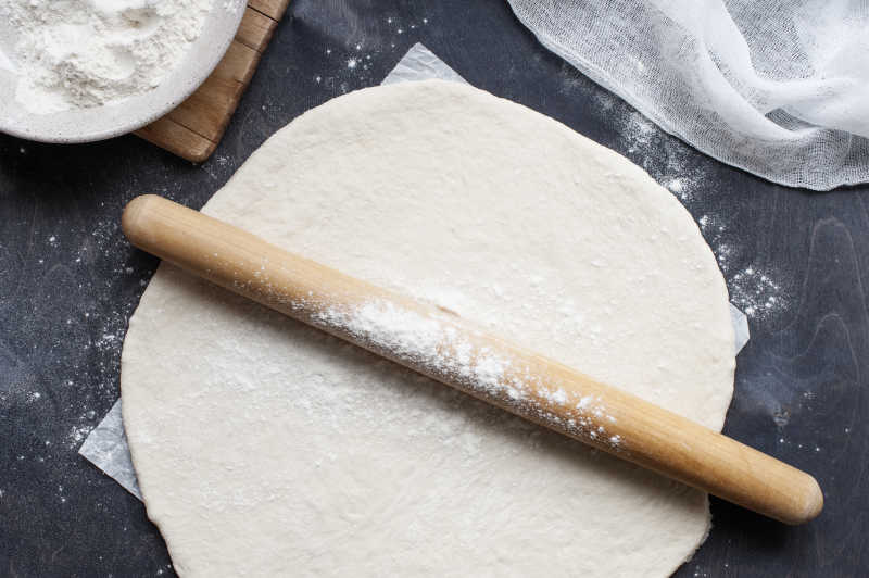 黑色背景下桌上擀面杖擀开的面团