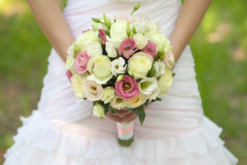 户外绿色草地背景下穿着婚纱的新娘手中美丽的手捧花