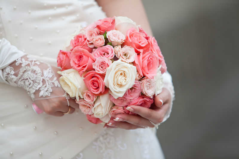 灰色背景下穿着白色婚纱的新娘手中的美丽婚礼花束