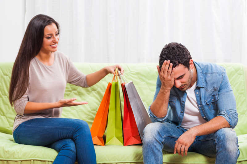 坐在沙发上用手按着脑门的男人和拿着购物袋的女人