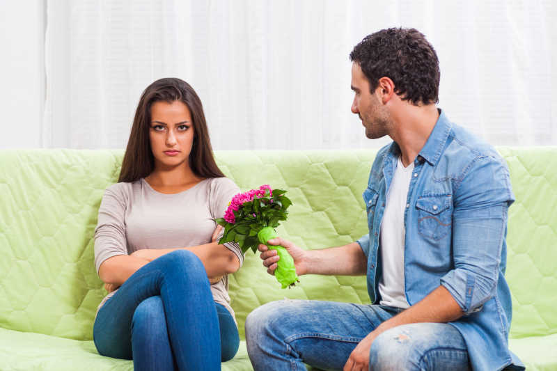 坐在沙发上男人用一束花哄生气的女人