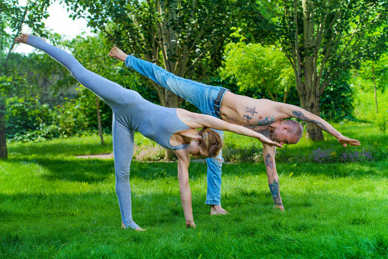 在绿色草坪上一起锻炼瑜伽的情侣