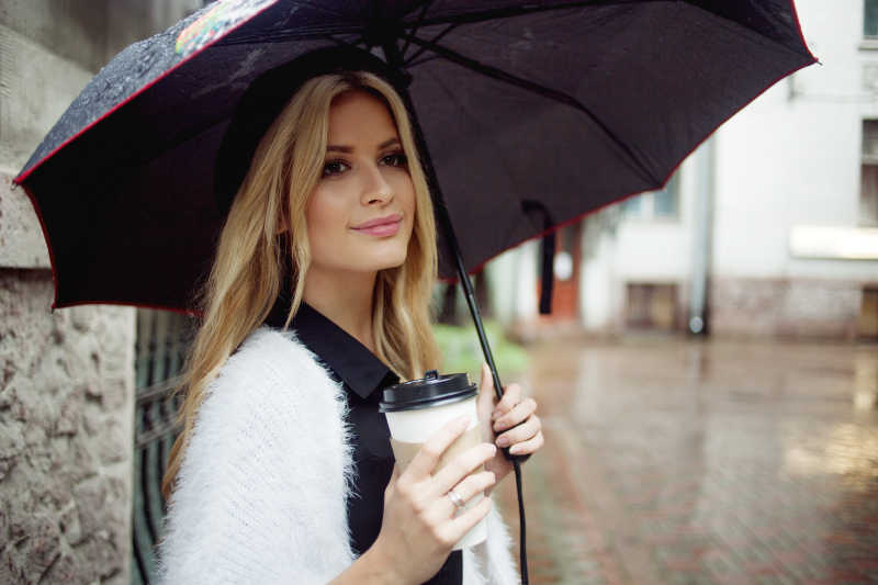 潮湿的路面上金发美女打着伞拿着咖啡