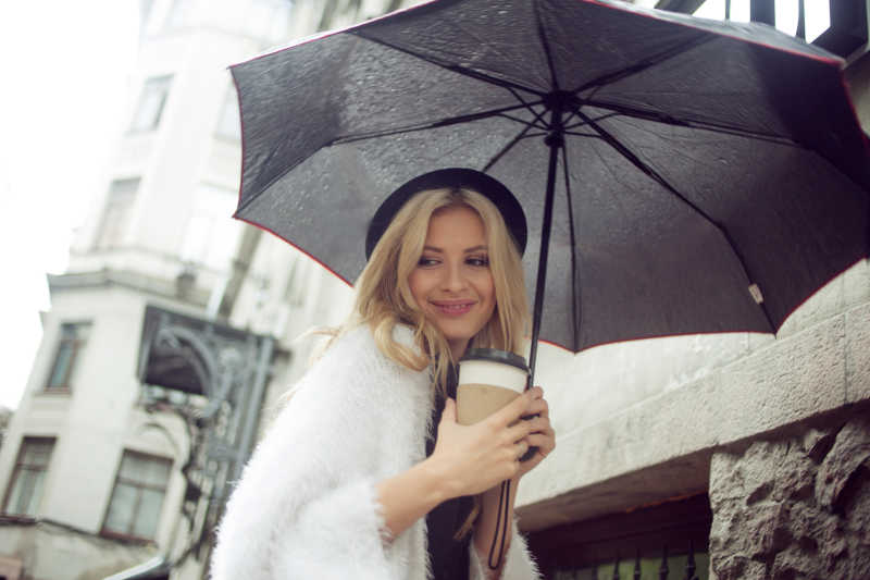 镜头下金发美女捧着咖啡打着雨伞