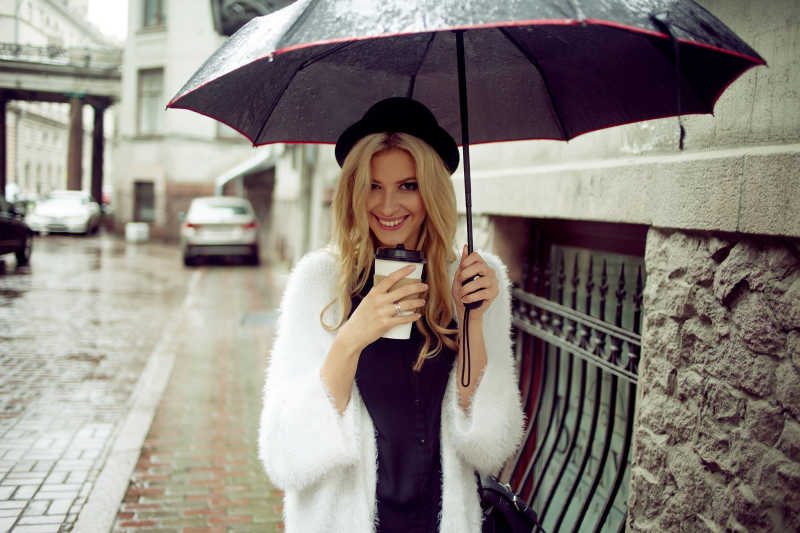 美丽的女人拿着咖啡打着伞