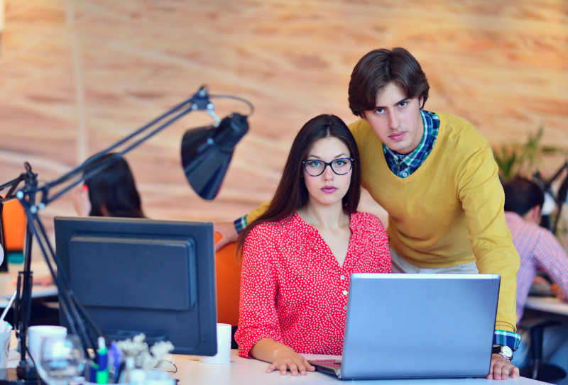 现代办公室背景下的对着笔记本讨论的同事