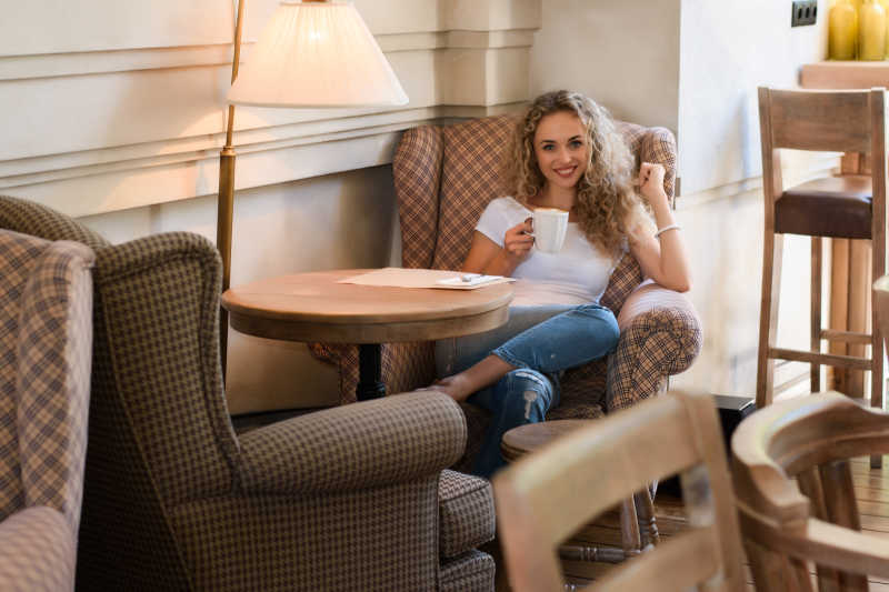 坐在沙发上的金发美女手拿一杯咖啡