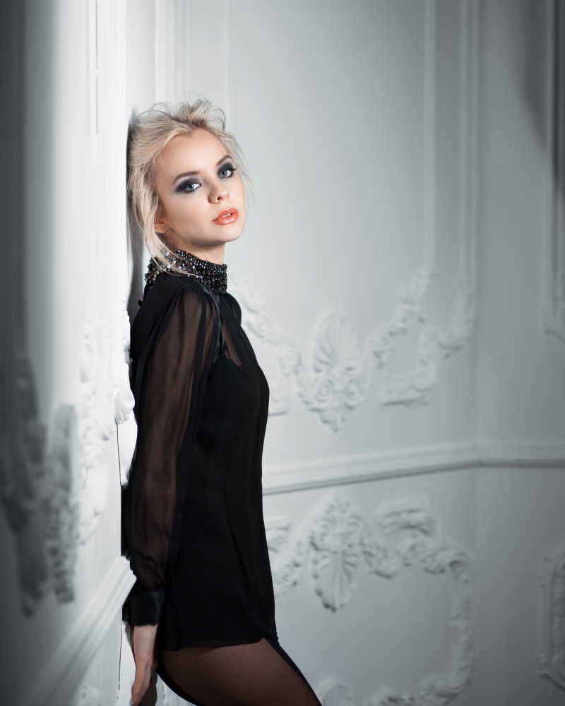 穿着黑色衣服靠在墙边的金发女郎