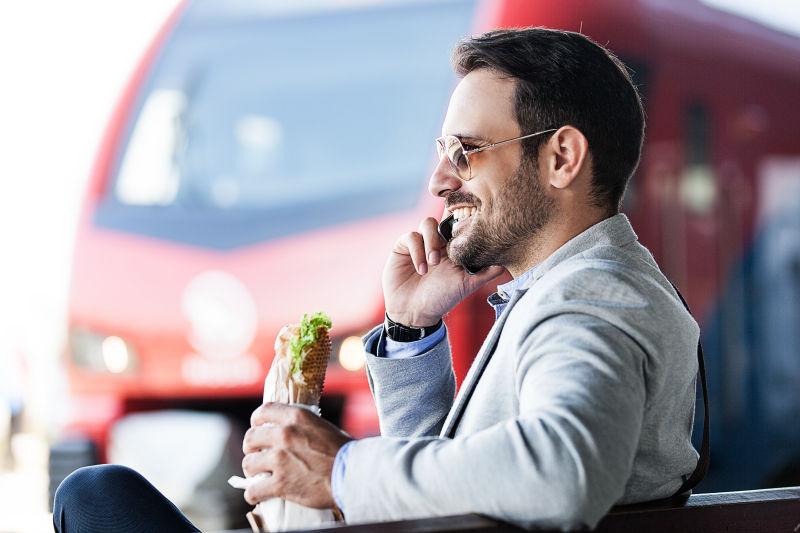 坐在火车站休息椅上边打电话边吃东西的男人