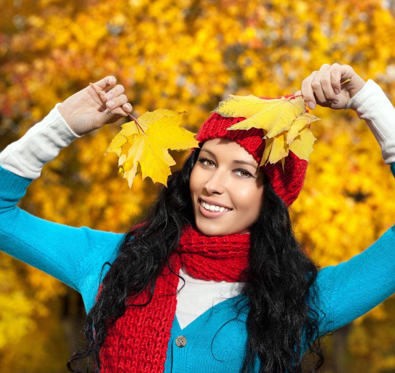 年轻白种女人在户外拿着金色的叶子