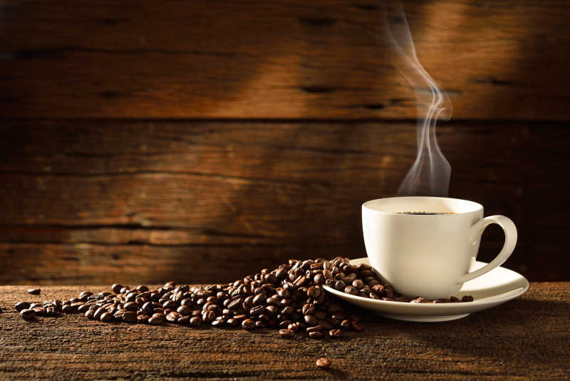 一杯冒着热气的咖啡与散落的咖啡豆放在木板上