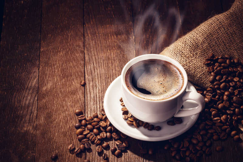 一杯冒着热气的咖啡与散落的咖啡豆