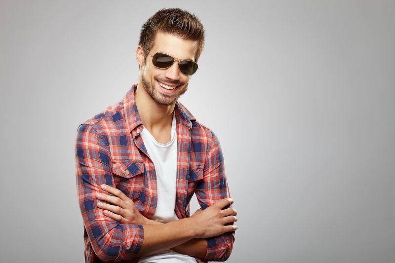 灰色背景下戴着太阳镜微笑的帅哥