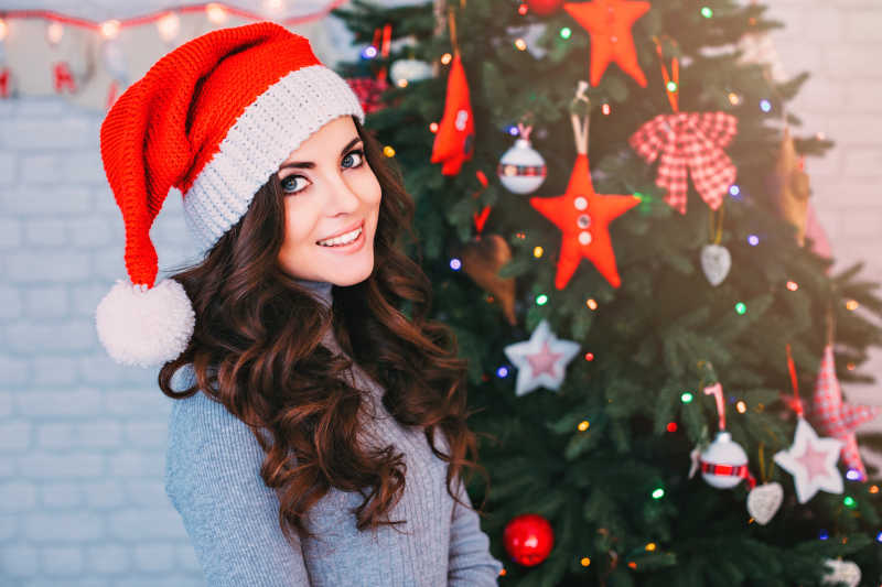 圣诞树背景前戴着圣诞帽的年轻美女