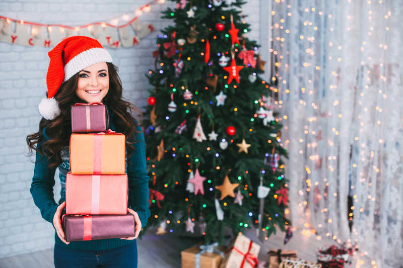 圣诞树背景前抱着礼盒的美女