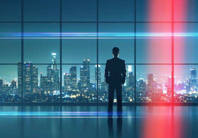 夜晚城市背景下商人站在落地窗前