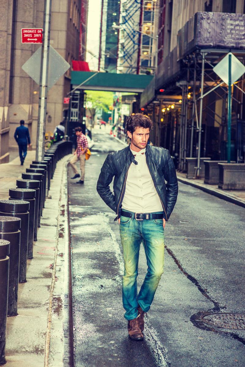 一个打扮时尚的男人在雨后在狭窄潮湿的街道上行走