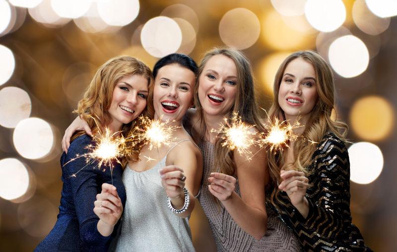 灯光背景下拿着烟火的微笑的女孩们