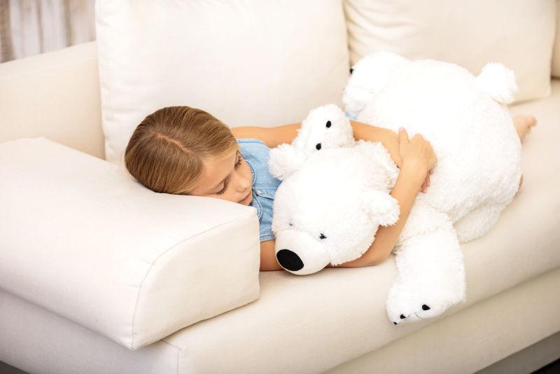 漂亮的小女孩躺在沙发上拥抱泰迪熊睡觉