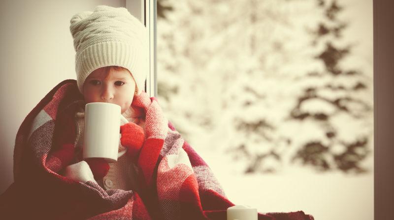 冬天穿着毛衣球的小女孩喝着一杯热茶
