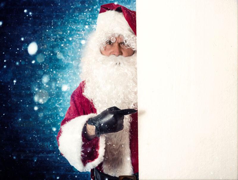 蓝色星空背景下指着空白板的圣诞老人