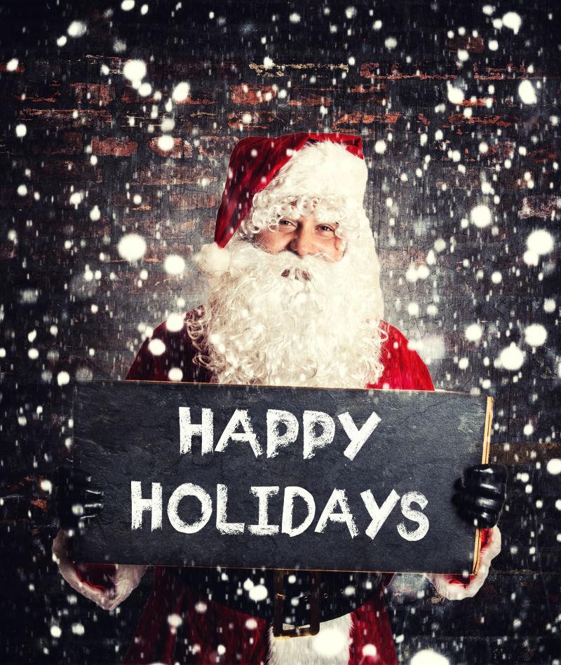 黑夜雪天背景下圣诞老人拿着写着字的黑板