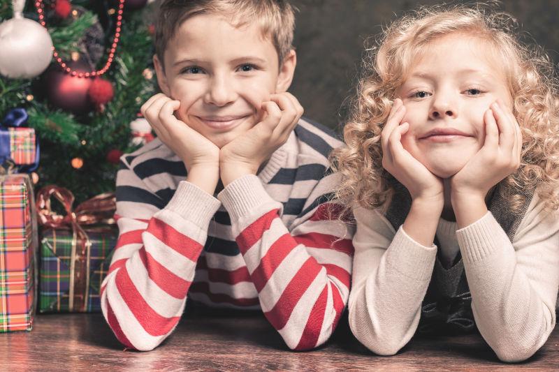 圣诞树背景下手撑着下巴趴在地板上的孩子们