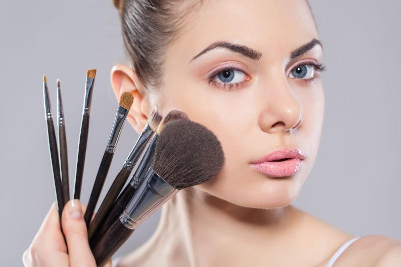 美丽的年轻女子拿着不同的化妆刷化妆