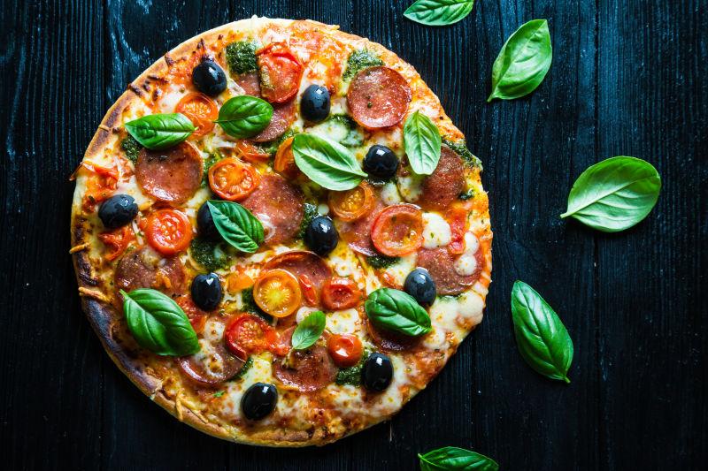 黑色背景下的意大利腊肠披萨橄榄和罗勒