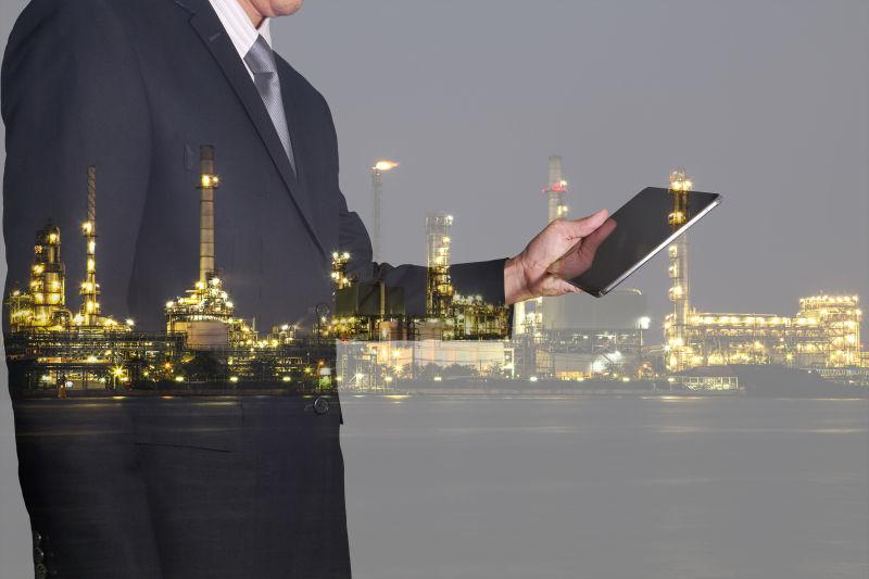 使用平板的商人和炼油厂夜景的双重曝光