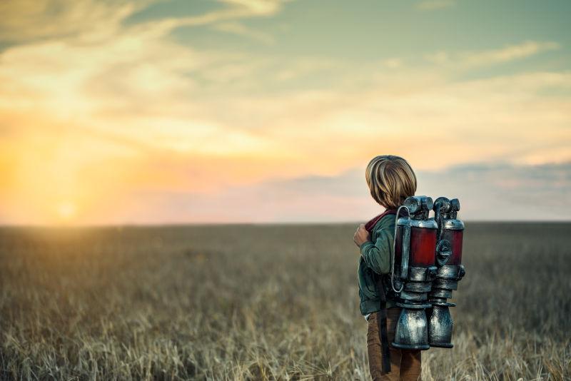在日落下背着喷气式飞行器的男孩