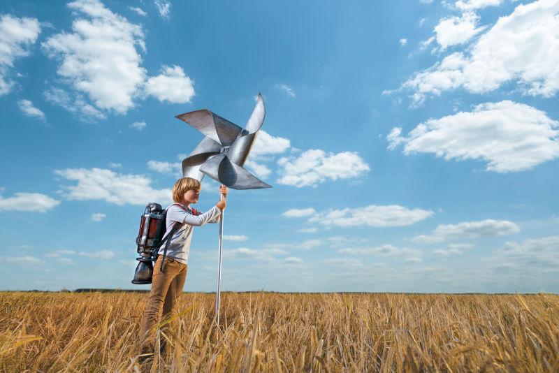 在户外背着喷气式飞行器和拿着风车的小男孩