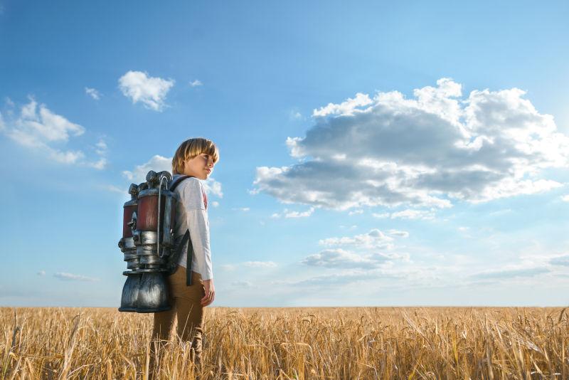 小男孩站在田野里背着喷气式飞行器